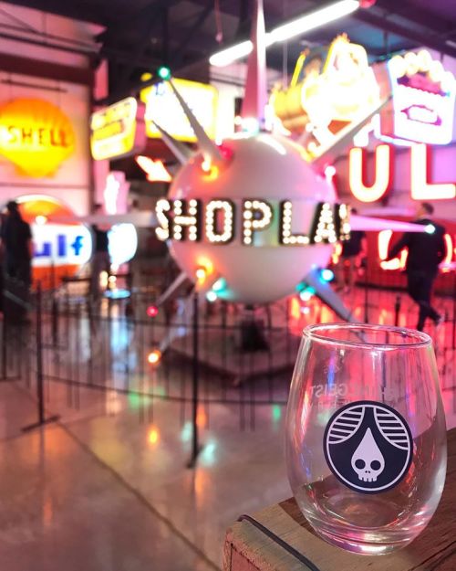 A glass with a logo in the foreground, colorful vintage neon signs in the background, and a central "SHOP" display.