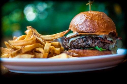 A juicy burger with melted cheese and lettuce, served with a side of golden French fries on a white plate.