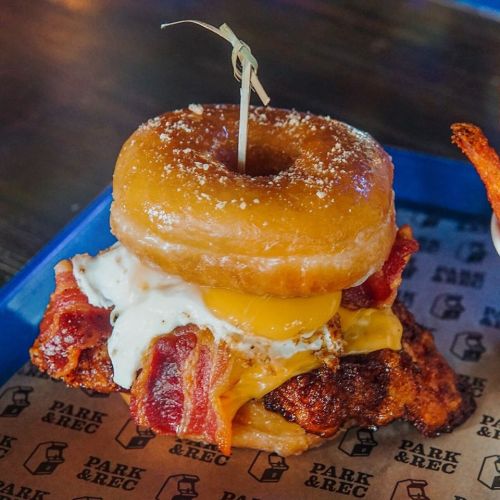 A sandwich featuring fried chicken, bacon, a fried egg, and a glazed donut on top, served on a blue tray.