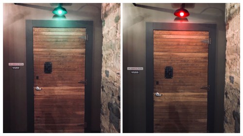 A wooden door with a small window, illuminated by a green light on one side and a red light on the other.