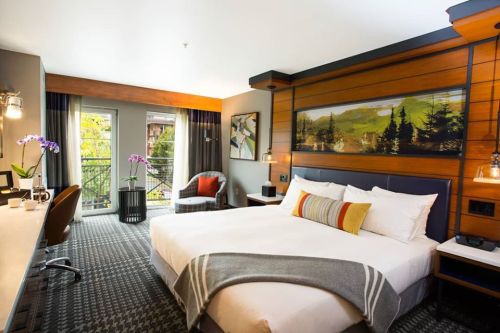 Modern hotel room with a king bed, stylish decor, balcony access, and a cozy seating area.