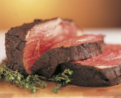 Sliced roast beef on a wooden board, garnished with fresh thyme, showcasing a juicy, tender interior.