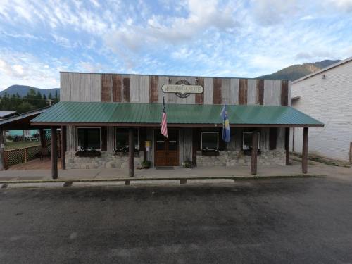 A rustic building with a green metal roof, featuring a sign, American flag, and mountain backdrop.