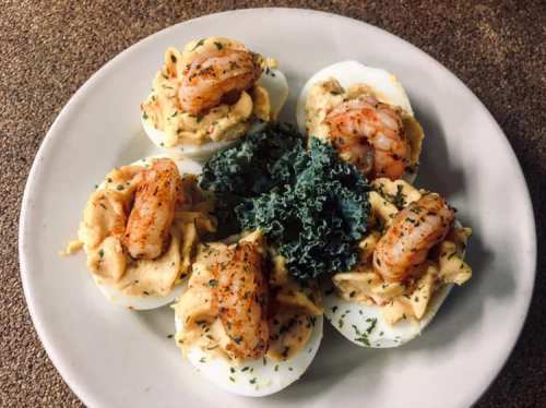 A plate of deviled eggs topped with shrimp and garnished with kale, sprinkled with herbs.