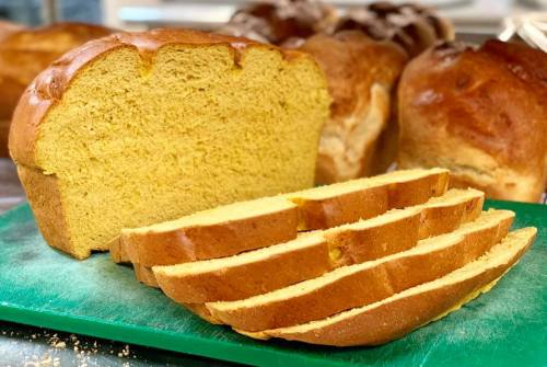 Freshly baked loaf of golden bread, sliced on a green cutting board, with whole loaves in the background.