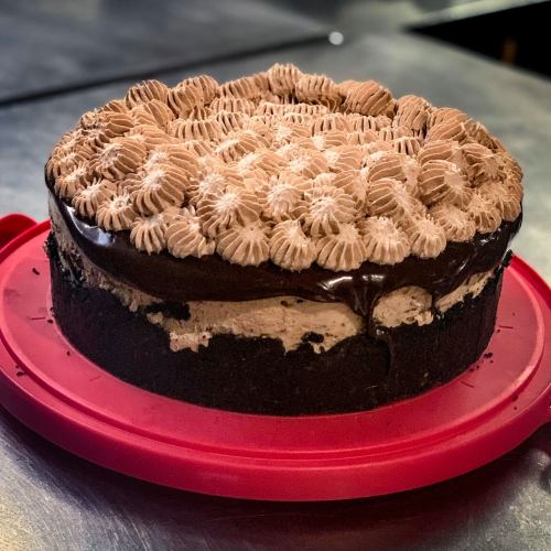 A round chocolate cake with swirled frosting on top, sitting on a red cake carrier.