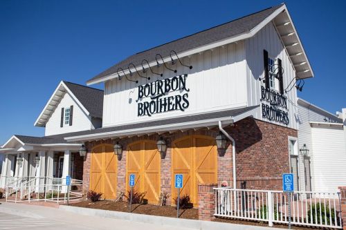 Exterior of Bourbon Brothers restaurant featuring a white and brick facade with wooden doors and a clear blue sky.