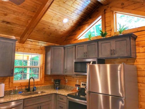 Cozy kitchen with wooden walls, gray cabinets, granite countertops, and large windows letting in natural light.