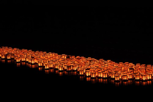 A serene night scene featuring glowing lanterns floating on water, creating a warm, reflective glow against the dark backdrop.