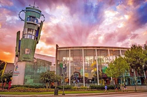 A modern building with a glass facade and a tall tower, set against a vibrant sunset sky.