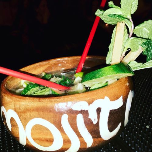 A close-up of a mojito in a decorative bowl, garnished with mint leaves and lime, featuring two red straws.
