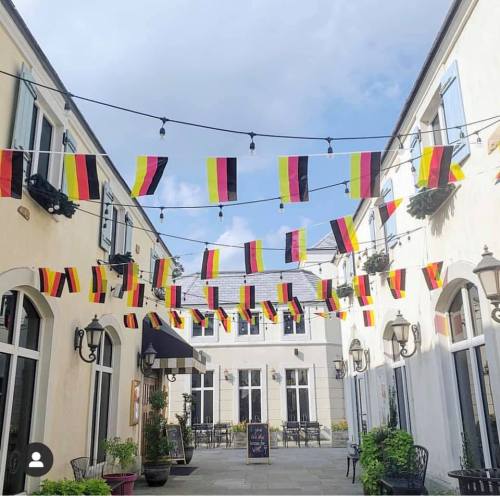 A charming courtyard decorated with black, red, and yellow flags, under a bright blue sky.