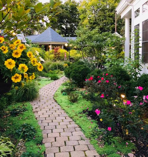A charming garden path lined with colorful flowers and greenery, leading to a gazebo in the background.
