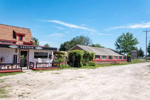 A quaint roadside establishment with a welcoming sign, surrounded by greenery and a clear blue sky.
