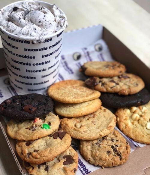 A box of assorted cookies with a cup of cookies and cream ice cream on top.