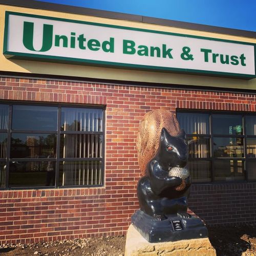 A large squirrel statue holding an acorn stands in front of the United Bank & Trust building.