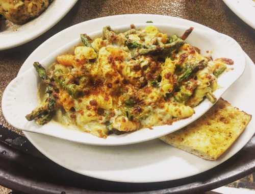 Baked pasta dish with asparagus, cheese, and breadcrumbs, served with a slice of toasted bread on the side.