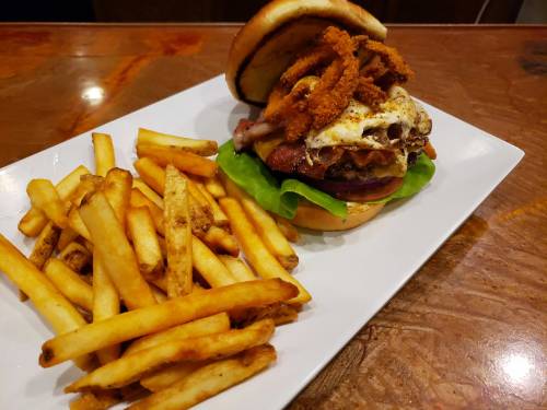 A hearty burger with lettuce, bacon, fried egg, and crispy onion rings, served with a side of golden French fries.