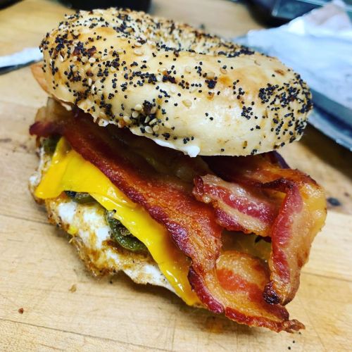 A toasted poppy seed bagel sandwich with bacon, cheddar cheese, and pickles.