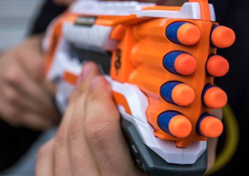 A close-up of a brightly colored toy blaster with orange and blue foam darts loaded in the chamber.