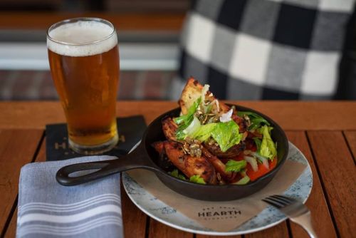 A cast iron skillet with a salad and roasted potatoes, alongside a pint of beer on a wooden table.