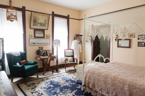 A cozy bedroom featuring a four-poster bed, vintage decor, a green armchair, and soft natural light.