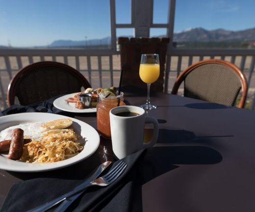 A breakfast table with eggs, sausage, hash browns, a drink, and a view of mountains in the background.