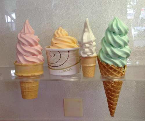 Five colorful ice cream cones and cups displayed on a shelf, featuring pink, orange, white, and mint green swirls.