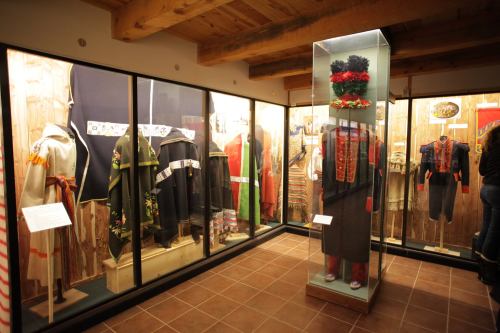 Display of traditional garments in glass cases, showcasing diverse cultural attire in a museum setting.