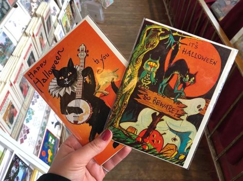 A hand holds two vintage Halloween cards featuring black cats, pumpkins, and spooky themes.
