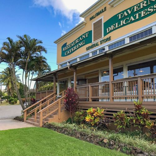 A colorful building with a restaurant and general store, surrounded by palm trees and lush greenery under a blue sky.