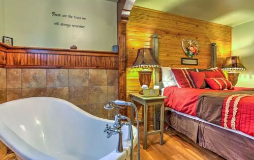 Cozy bedroom with a wooden accent wall, a large bed, and a vintage bathtub nearby, creating a warm, inviting atmosphere.