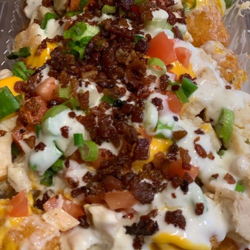 A close-up of loaded nachos topped with cheese, bacon, tomatoes, green onions, and drizzled with sour cream.