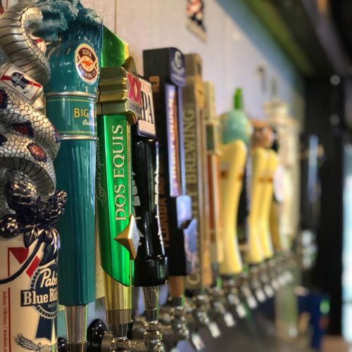 A row of colorful beer taps featuring various brands and styles in a bar setting.