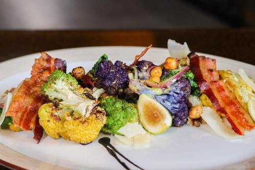 A colorful plate of roasted vegetables, including broccoli, cauliflower, and bacon, garnished with nuts and lemon.