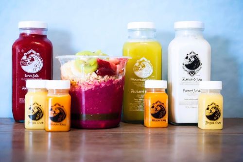 A colorful display of juices and a smoothie bowl, featuring vibrant fruits and granola, on a wooden table.