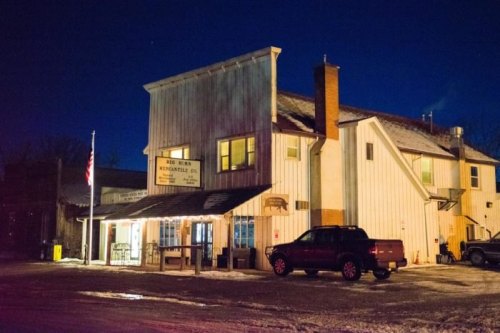 A rustic building at night with a flag, featuring a sign for "Big Man's" and a parked vehicle in front.