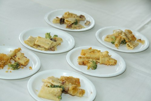 Plates of rigatoni pasta with broccoli and creamy sauce, garnished with breadcrumbs, arranged on a table.