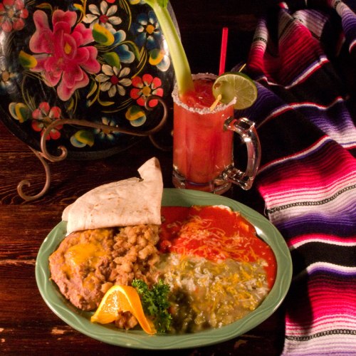 A colorful plate of Mexican food with beans, cheese, rice, a tortilla, and a vibrant drink on a striped blanket.