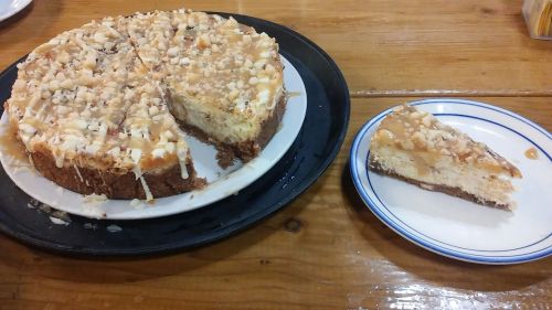A round cheesecake topped with caramel and nuts, with a slice cut out on a plate beside it.