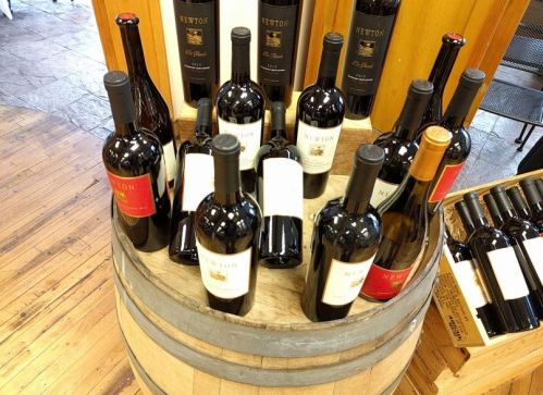 A wooden barrel displays various bottles of red wine, including several labeled "Newton."