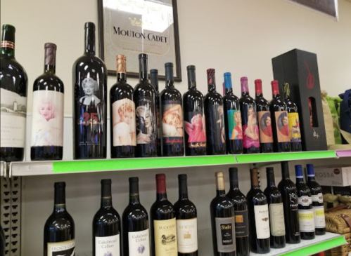 A shelf displaying various wine bottles with artistic labels featuring colorful portraits and designs.