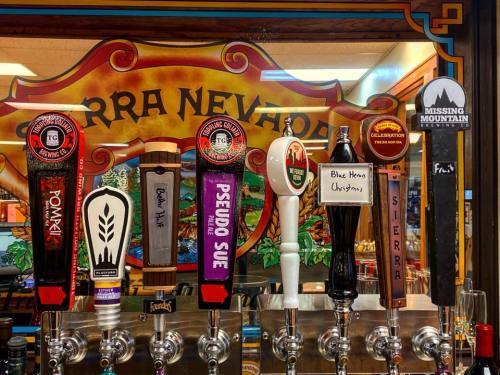 A row of beer taps featuring various brands and styles against a colorful Sierra Nevada backdrop.