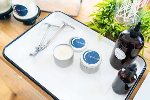 A tray with candles, a candle snuffer, and dark glass bottles, surrounded by greenery.