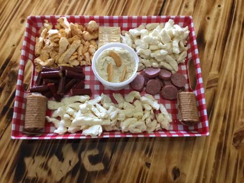A tray with assorted snacks: crackers, cheese puffs, meat sticks, and a bowl of dip, arranged in a checkered pattern.