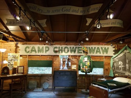 Interior of Camp Chowenwaw, featuring wooden walls, a large sign, and displays of camp memorabilia and uniforms.