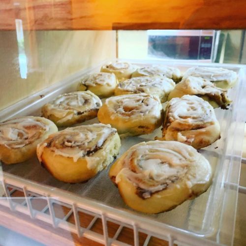 A tray of freshly baked cinnamon rolls with creamy icing, displayed in a glass case.