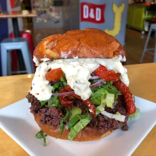 A close-up of a hearty sandwich with beef, lettuce, sun-dried tomatoes, and creamy sauce on a toasted bun.