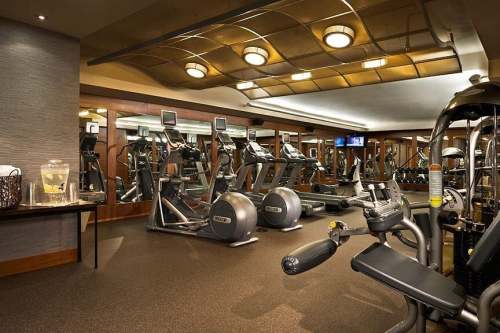 A modern gym with exercise equipment, mirrors, and a water station, featuring cardio machines and weights.