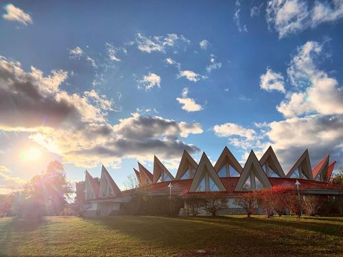 A unique building with triangular roofs under a blue sky with clouds, illuminated by the setting sun.
